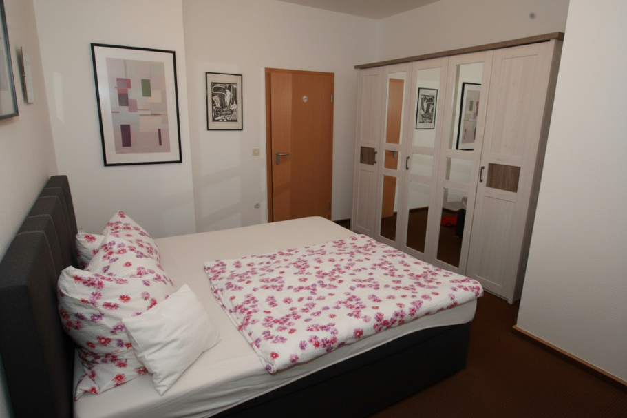 Helles Schlafzimmer mit einem Bett, bunten Kissen und einem Kleiderschrank.